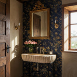 Beige travertine fluted D-shape console sink with hand-carved stone detail and black metal stand.