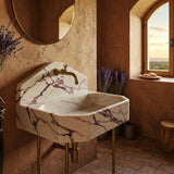 Octagonal Calacatta Viola marble console sink with brass legs and elegant peaked backsplash.