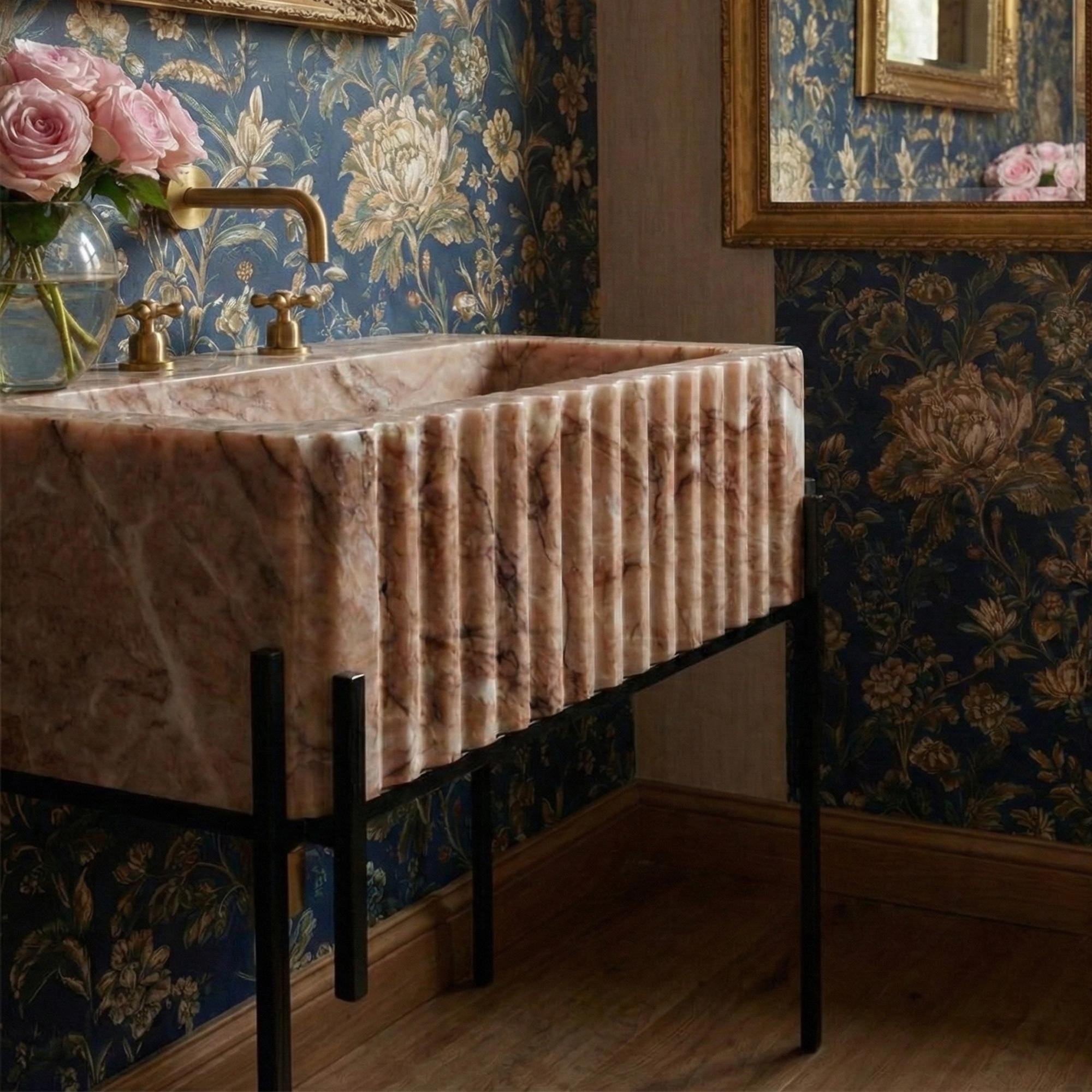Luxurious hand-carved fluted vanity sink made from Pink Viola marble with vintage brass faucet and black stand.